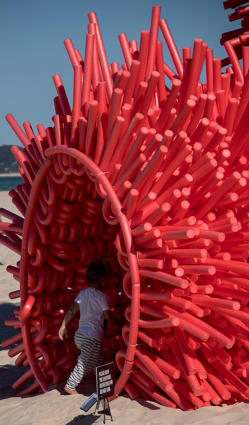 Child Entering Giant Red Foam Sculpture on Beach
