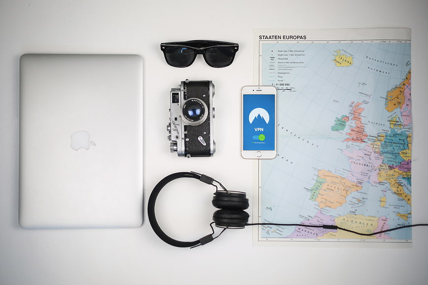 Flat lay of travel essentials with laptop, camera, map, and VPN smartphone