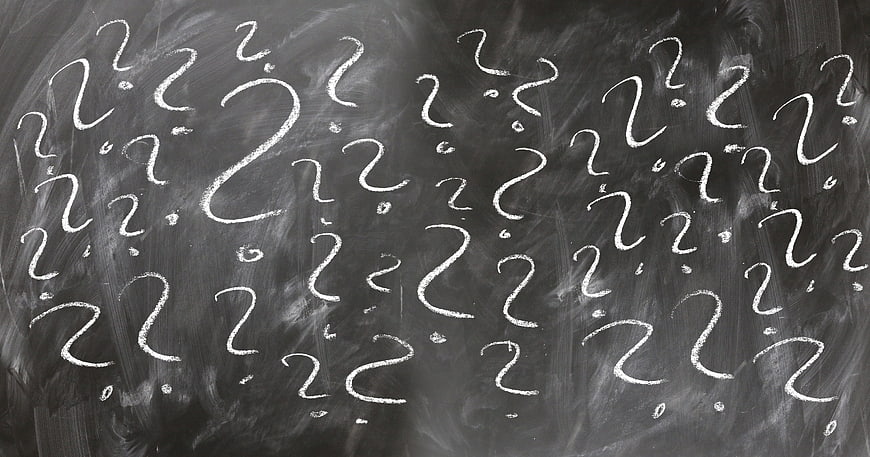 White chalk question marks on a dark blackboard background