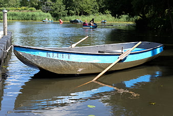 Blue wooden rowboat docked at a calm lake with people rowing in background