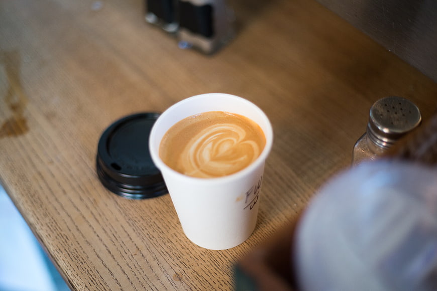 Latte art heart in white paper coffee cup on wooden table