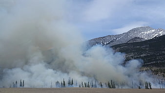 Thick Smoke Rising from Forest Fire Near Snowy Mountain