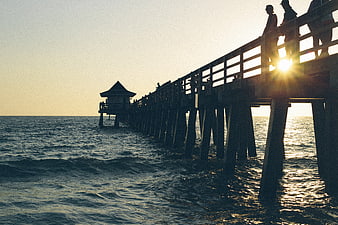Silhouetted pier at sunset with people fishing and walking