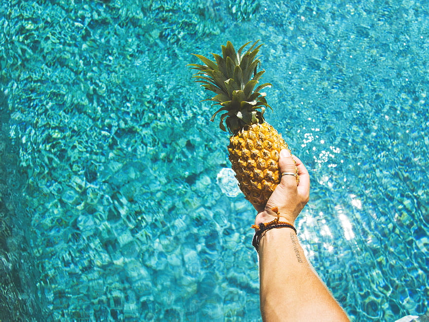 Hand holding pineapple over blue swimming pool water