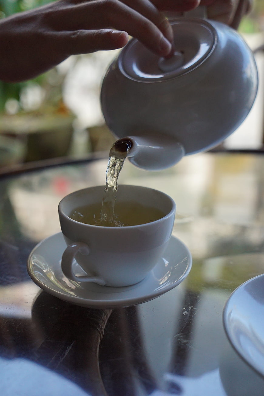 Pouring Hot Tea into White Cup on Glass Table