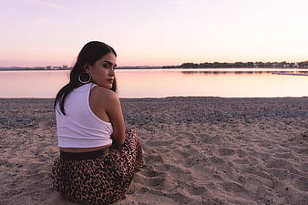 Woman Sitting on Sandy Beach at Sunset