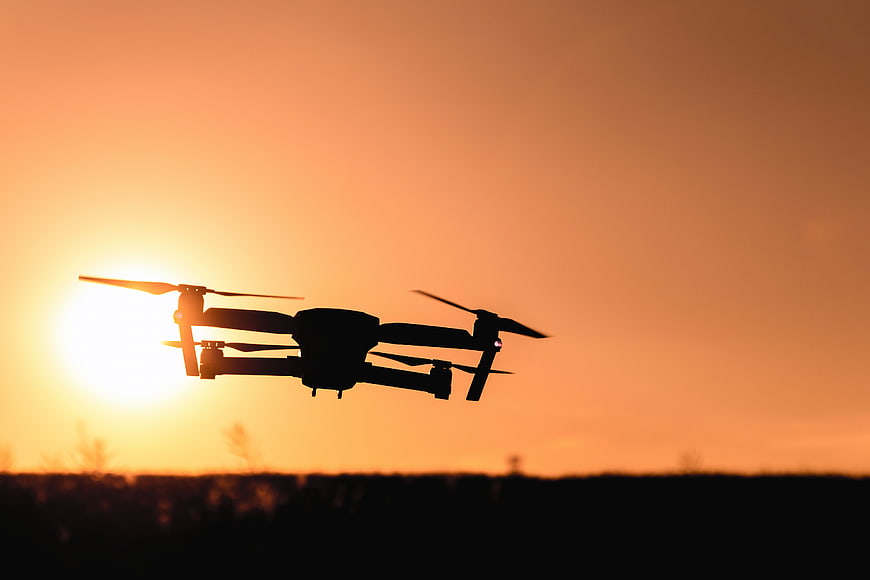 Silhouette of Drone Flying Against Orange Sunset Sky