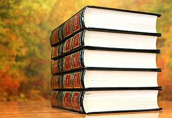 Stack of five hardcover books on wooden table with autumn background