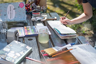 Woman painting outdoors with watercolors on wooden table