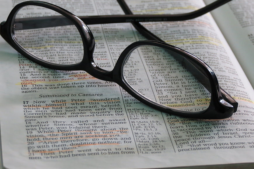 Black Glasses Resting on Open Bible Text