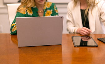 Two female professionals working on laptop and tablet at office desk