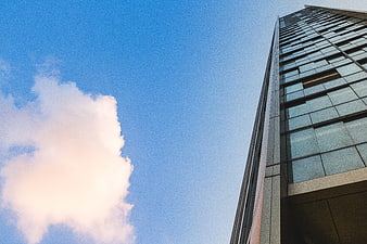 Low-angle view of modern glass skyscraper against blue sky