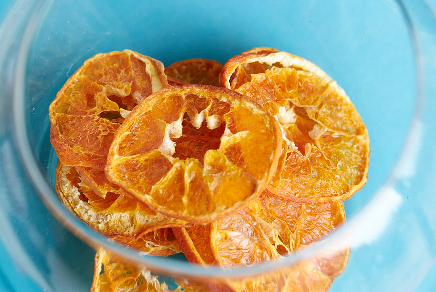 Dried Orange Slices in Glass Bowl on Blue Background