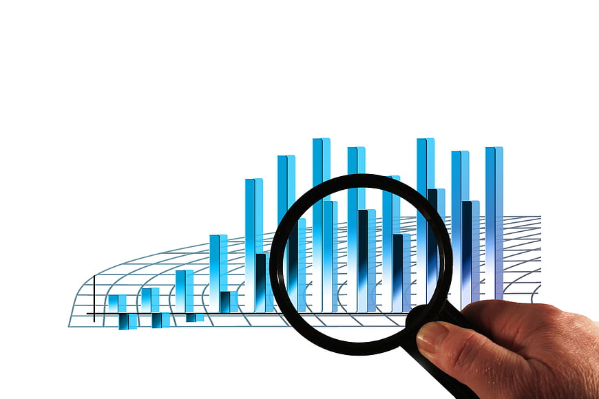 Hand holding magnifying glass over blue 3D bar chart