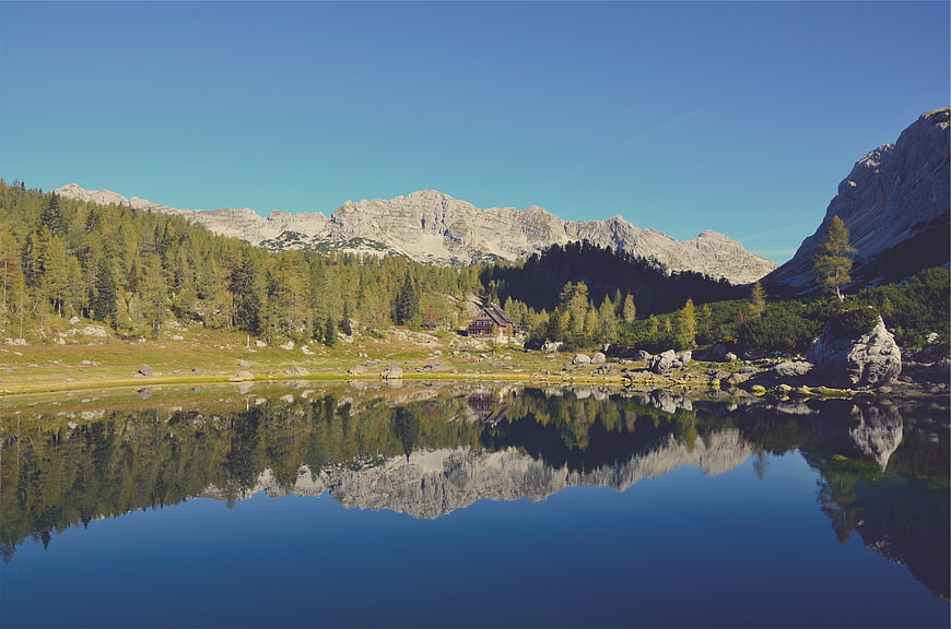 Serene Alpine Lake with Mountain Reflection and Wooden Cabin