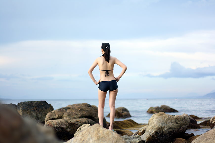 Woman in Black Swimsuit Standing on Rocks by Ocean