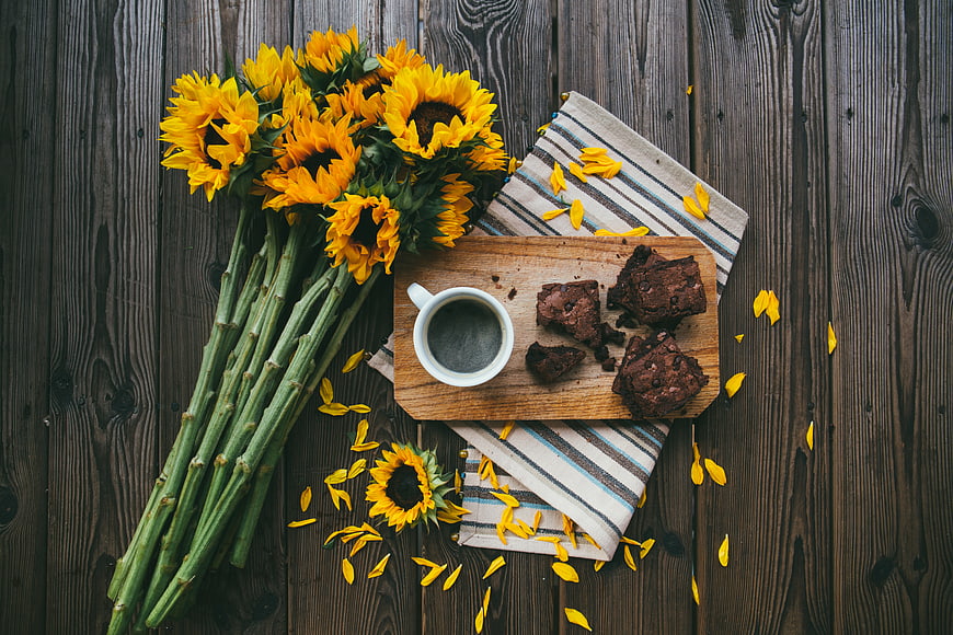 Flat lay of sunflowers, coffee, and brownies on rustic wood