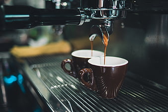 Espresso pouring into two brown ceramic cups from machine