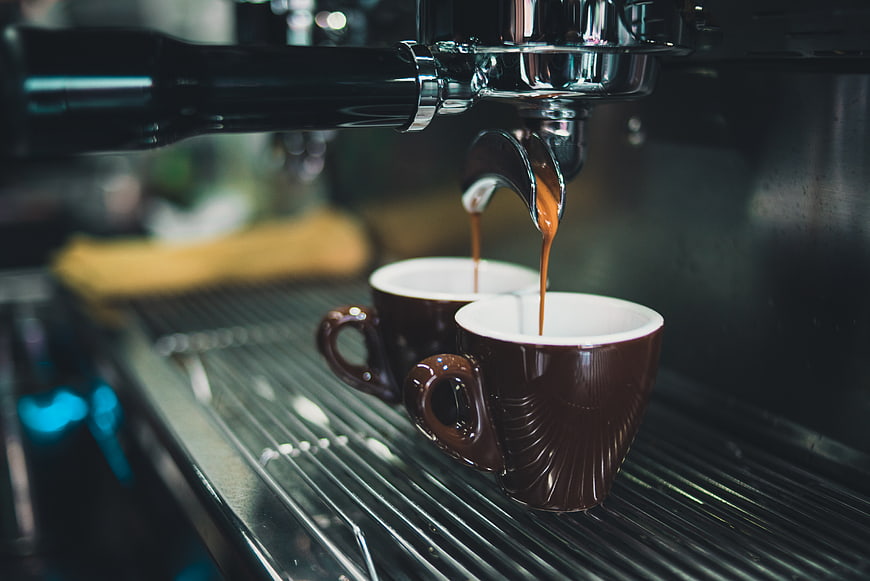 Espresso pouring into two brown ceramic cups from machine