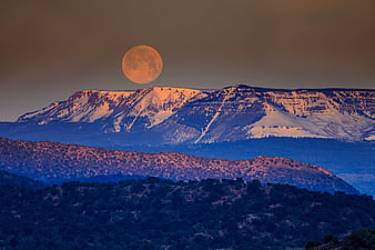 Full Orange Moon Rising Over Snow-Capped Mountain Range at Sunset