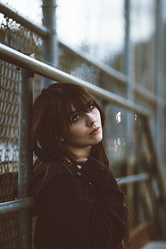 Cinematic portrait of young woman leaning against chain link fence
