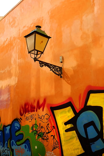 Vintage street lamp on orange wall with graffiti