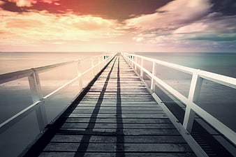 Wooden pier extending into calm ocean at sunset with dramatic sky