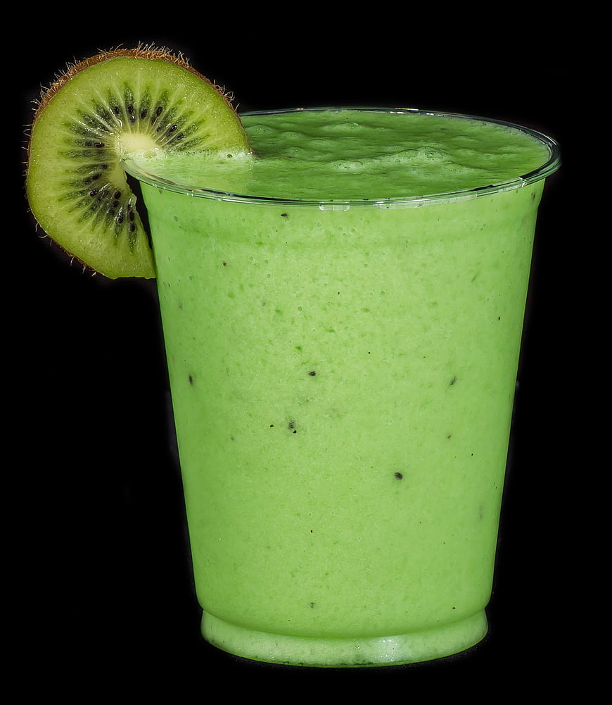 Green Kiwi Smoothie in Glass with Fresh Slice Garnish on Black Background