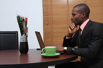 African businessman in suit thinking at office desk with laptop and coffee
