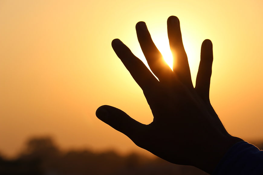 Silhouette of Hand Reaching for Sun at Sunset