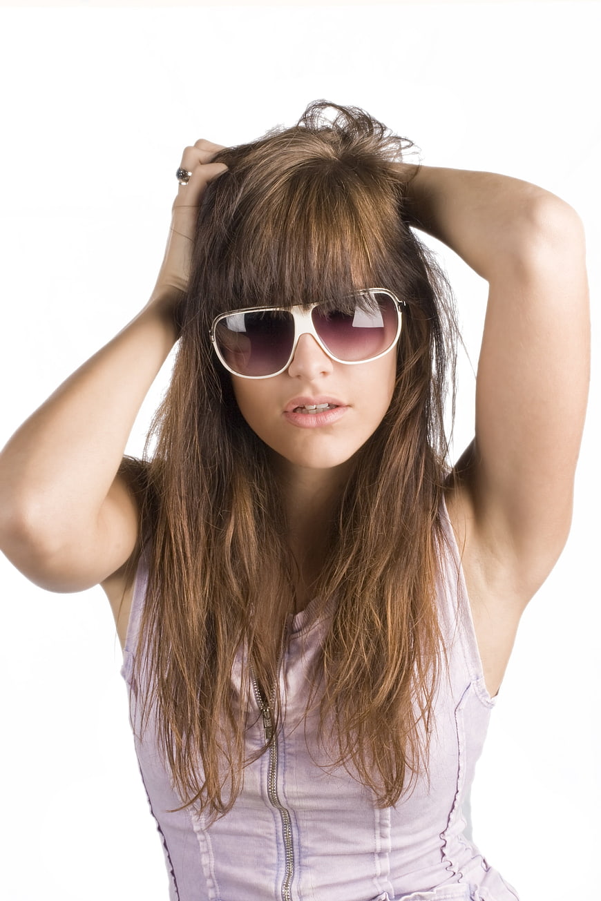 Young woman with long brown hair and white sunglasses posing against white background