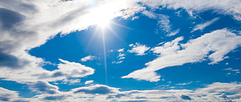 Bright Sun Shining Through White Clouds in Blue Sky