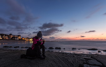 Child Sitting on Beach at Sunset Looking at Phone