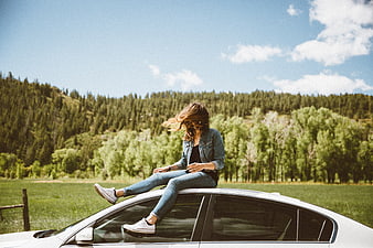 Woman sitting on car roof in nature landscape