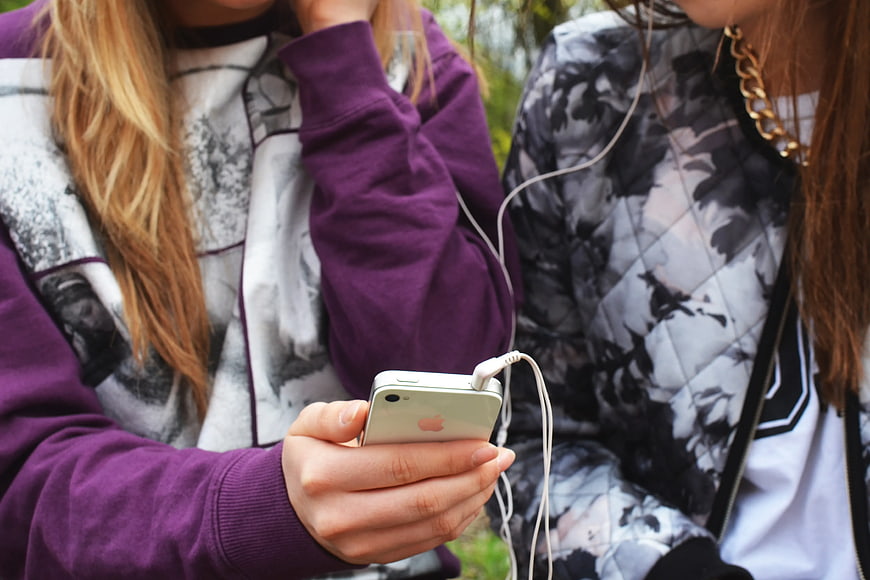 Two women sharing earphones listening to music on smartphone