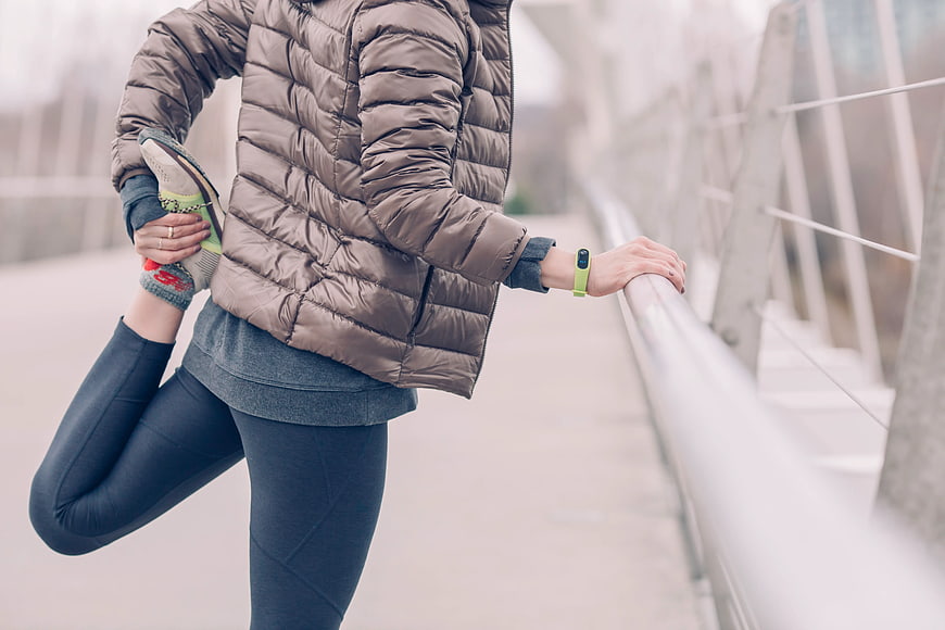 Woman stretching leg in puffer jacket on bridge