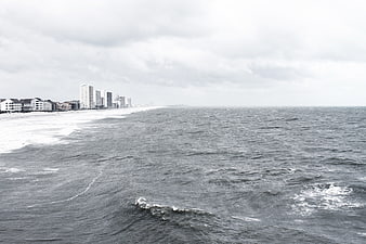 Overcast coastal cityscape with ocean waves and high-rise buildings