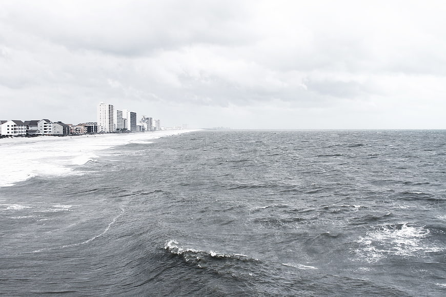 Overcast coastal cityscape with ocean waves and high-rise buildings