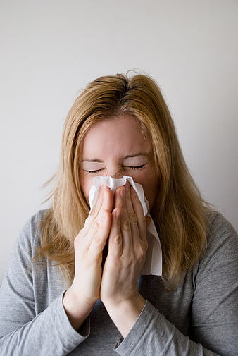 Woman Blowing Nose with Tissue Against White Background