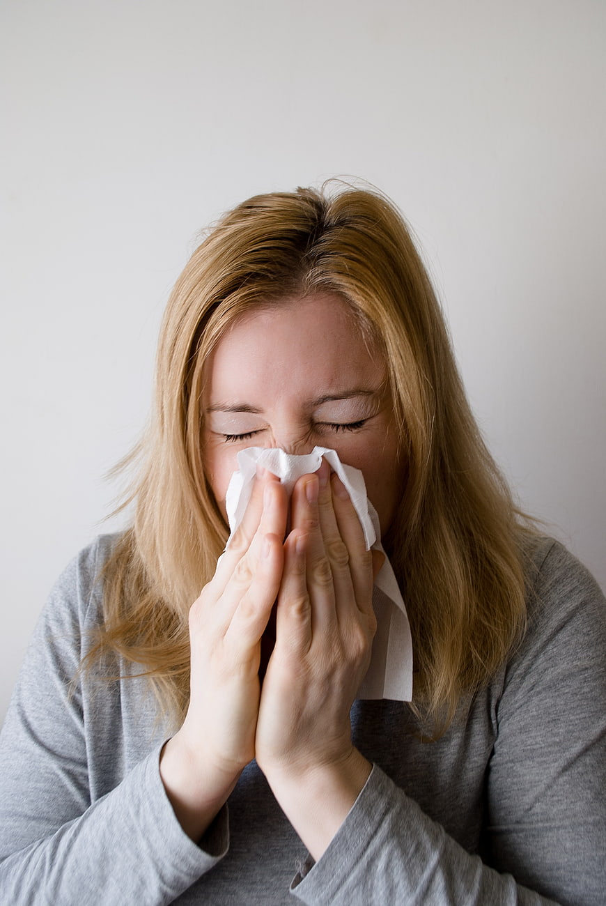 Woman Blowing Nose with Tissue Against White Background