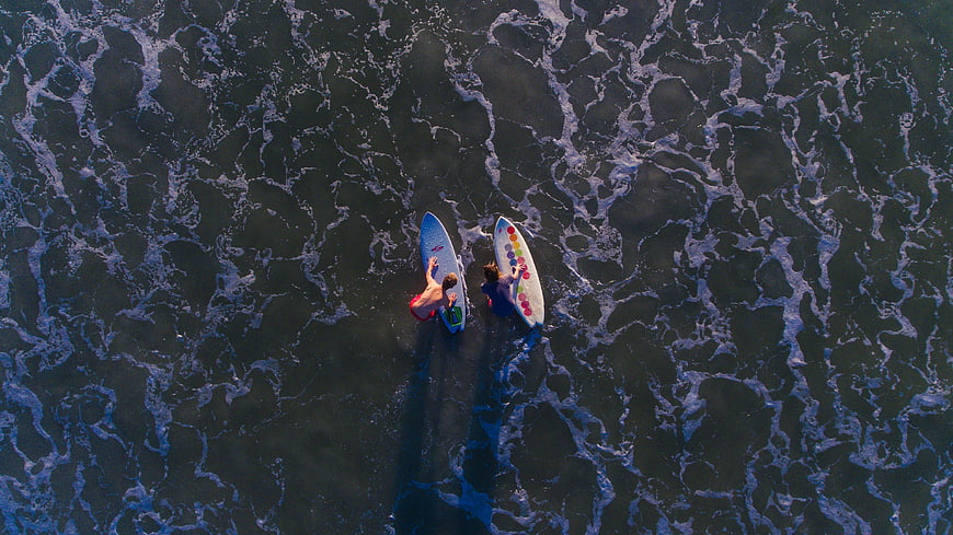 Aerial view of two surfers paddling in ocean waves