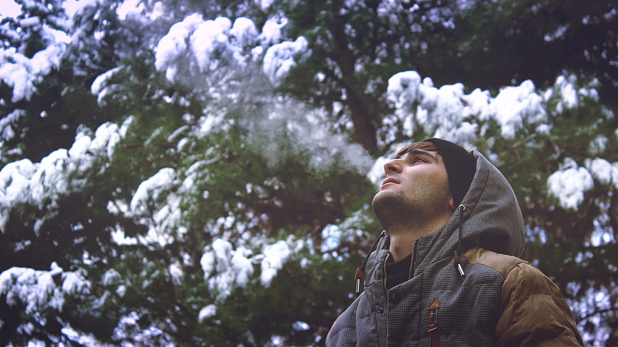 Young Man Looking Up at Snowy Pine Trees in Winter