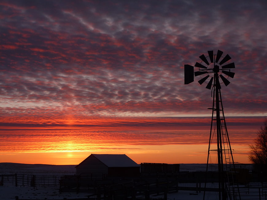 Silhouette of windmill and barn against dramatic red sunset sky