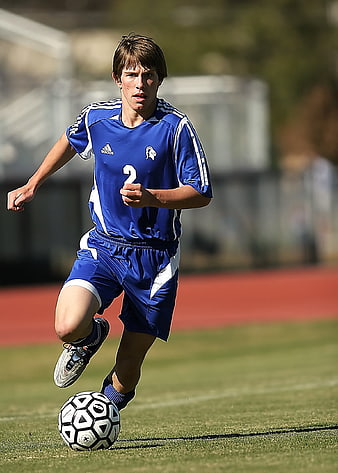 Young male soccer player dribbling ball on grass field