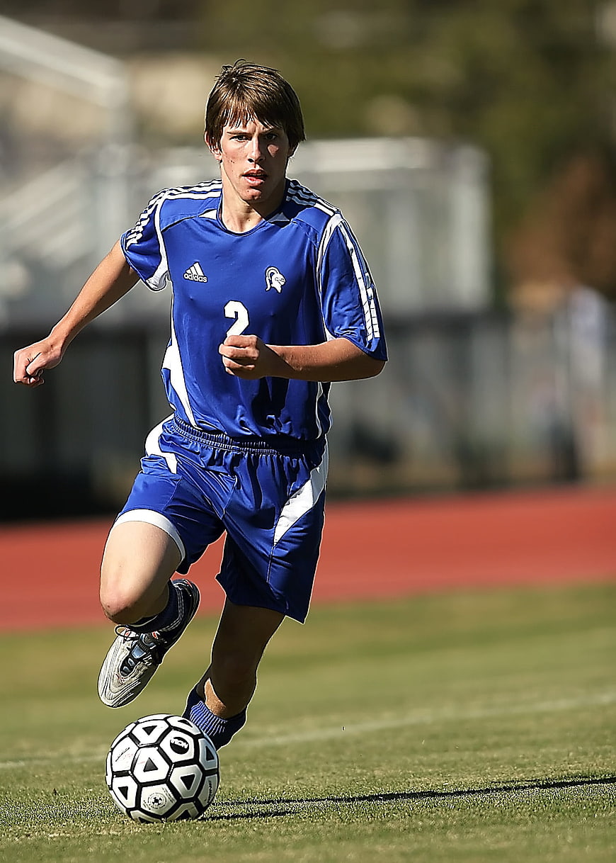 Young male soccer player dribbling ball on grass field