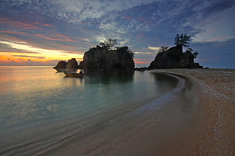 Serene Sunset Beach with Rocky Outcrops and Moored Boat