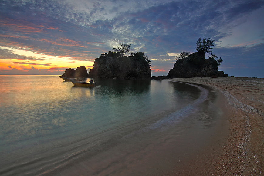 Serene Sunset Beach with Rocky Outcrops and Moored Boat