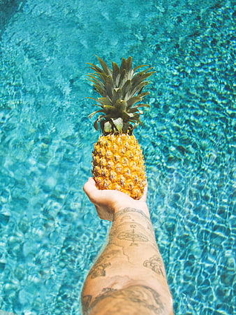 Hand holding pineapple over blue swimming pool water