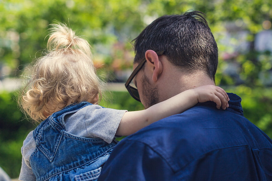 Father holding toddler daughter outdoors in park