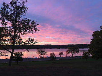Vibrant pink and purple sunset over a calm lake with silhouetted trees